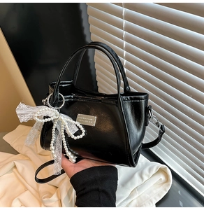 Close-up of black PU leather handbag featuring a pearl bow and lace ribbon charm