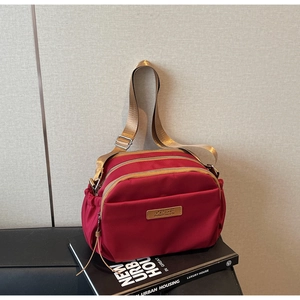 Detail view of red multi-layer nylon crossbody bag with three gold zippers and logo