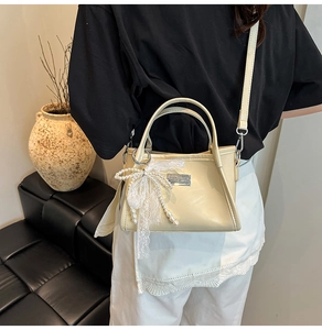Detail of beige shoulder bag with lace bow charm and silver plaque on a leather sofa