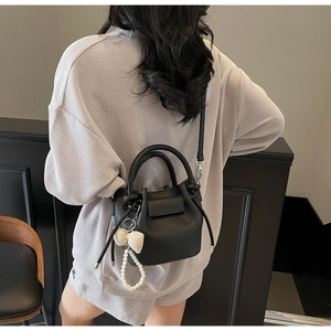 Detail of black lychee grain bucket bag with pearl bow charm worn by a model