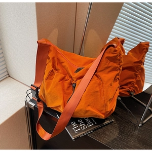 Detail showing the side drawstring pocket and wrinkled nylon texture of the orange hobo bag