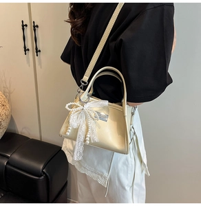 Detail of cream shoulder bag featuring lace bow and pearl charm with silver hardware