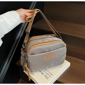 Detail of grey nylon crossbody bag with three zipper compartments and adjustable strap