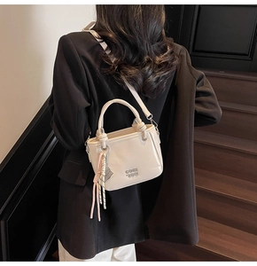 Vue détaillée du sac seau blanc crème avec lettres en métal et pendentif tissé