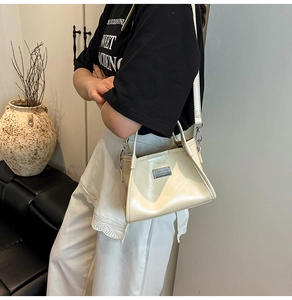 Detail shot of a cream-white glossy bow shoulder bag with silver hardware on a model