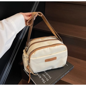 Close-up of beige nylon crossbody bag featuring three zippered pockets and brown straps