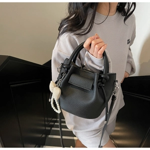 Detail of black pebbled leather bucket bag with pearl charm on minimalist stairs