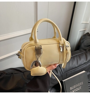 Detail of cream Boston bag with heart charm and silver hardware on a black leather sofa