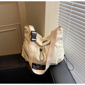 Minimalist beige nylon hobo bag featuring wide adjustable strap and drawstring detail