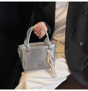 Détail du sac seau argenté texturé avec logo métallique et pendentif en corde tressée