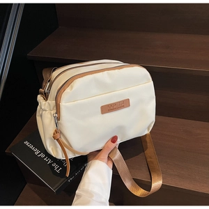 Detail of cream nylon crossbody bag with multiple zip pockets and adjustable brown strap