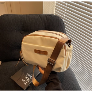 Detailed view of cream nylon crossbody bag showing three main zipper compartments and side pleats