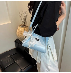 Detail of light blue shoulder bag featuring delicate white lace bow and pearl pendant charm