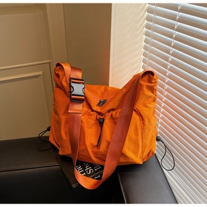 Detailed macro view of orange nylon crossbody bag with side drawstring and plastic buckle