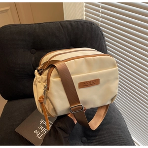 Detail view of cream nylon crossbody bag with three metal zippers and brown strap