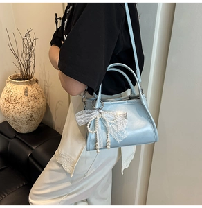 Detail of light blue faux leather bag with lace bow and hanging pearl decorations