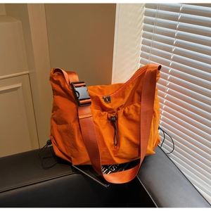 Close-up of orange pleated nylon crossbody bag featuring large black plastic buckle and strap