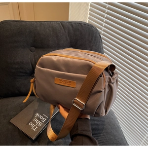 Detail view of coffee nylon crossbody bag showing multi-layered zippers and wide strap
