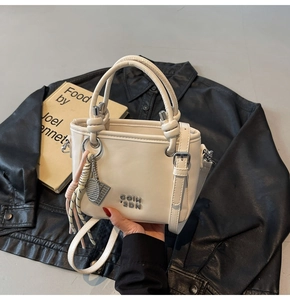 Détail du sac à main en cuir PU crème avec logo métallique et pendentif décoratif