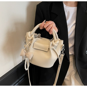 Detail of cream white pleated bucket bag with lychee texture and pearl bow charm