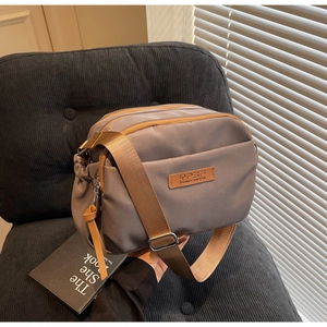 Detail of grey nylon crossbody bag with three zip compartments and wide brown strap