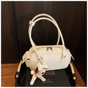 Détail du sac boston blanc crème avec pendentif chiot en peluche sur fond bois sombre