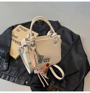 Détail du sac seau beige avec logo en métal, breloque tressée et bandoulière sur du cuir