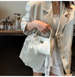Detail of white bow shoulder bag with pearl charm and sleek silver buckle finish