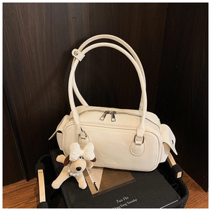 Détail d'un sac oreiller crème en cuir brillant avec poches et breloque peluche