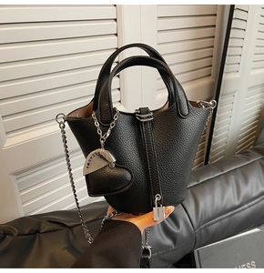 Detail of black lychee grain leather bucket bag with silver chain and heart pendant