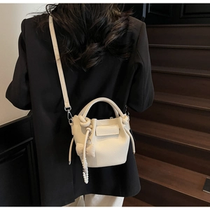 Detail of cream lychee leather bucket bag with pearl tassel and bow on a model