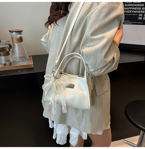 Detail of cream shoulder bag featuring elegant lace bow pendant and pearl accents