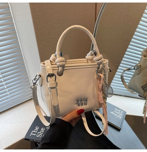 Détail du sac seau crème avec lettrage argenté, breloque tennis et poignée en foulard de soie