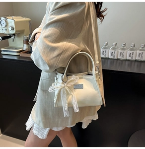 Detail of cream white faux leather shoulder bag with pearl bow charm and metal plaque