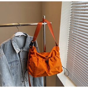 Detail view of bright orange nylon dumpling bag with drawstring and adjustable strap
