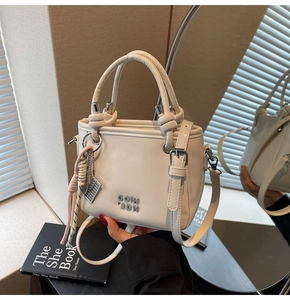Gros plan du sac à main beige avec logo métallique et pendentif boulier décoratif
