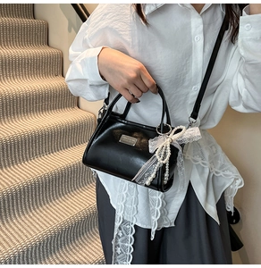 Detail of black bow bag with lace and pearls worn on a shoulder against stairs
