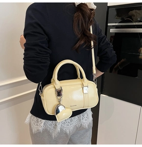 Close-up of a cream yellow glossy Boston bag with a heart charm and strap on a model