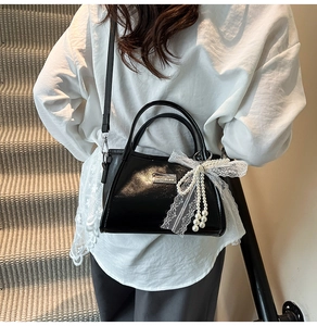 Detail of black patent leather underarm bag featuring a lace bow and pearl charms
