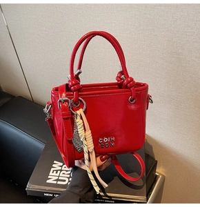 Detail der roten Kunstleder-Handtasche mit Metall-Logo und gewebtem Anhänger