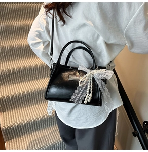 Detail of black bow shoulder bag featuring white lace and elegant pearl charm accessories