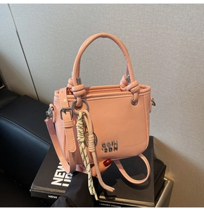 Rosa Eimertasche mit Metalllogo und geflochtenem Anhänger auf einem Buch