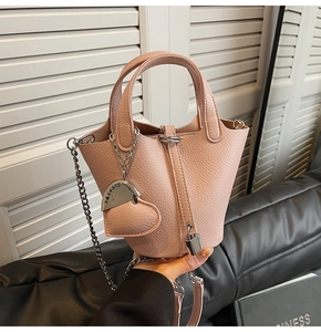 Detail of pink lychee leather bucket bag with heart pendant and metal chain strap