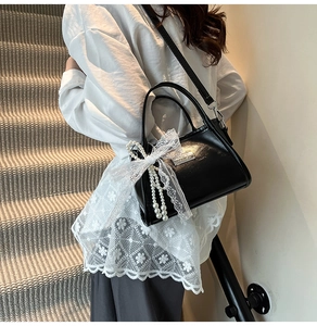 Detail of black glossy leather shoulder bag with white lace bow and pearl charms