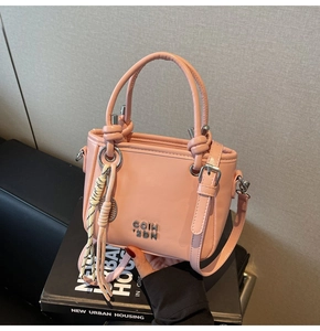 Détail du mini sac seau rose avec logo argenté et breloque sur un livre noir