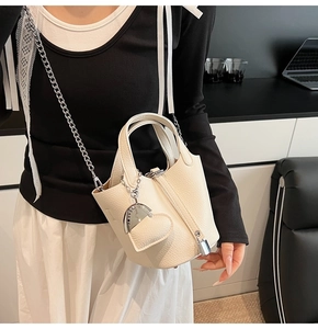 Close-up of the silver heart-shaped pendant with CLEARLY engraving on a cream leather bucket bag