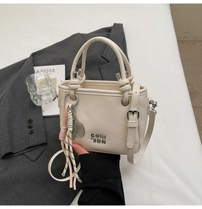 Gros plan du sac seau crème avec logo métallique et breloque raquette sur costume