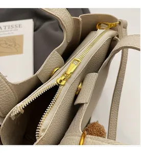 Detail of beige litchi leather tote bag featuring gold zipper and brown plush charm