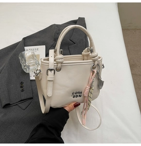 Détail du sac seau en cuir PU blanc cassé avec logo en métal et breloque tissée rose