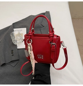 Gros plan du sac seau en cuir verni rouge avec lettrage argenté et détails métalliques
